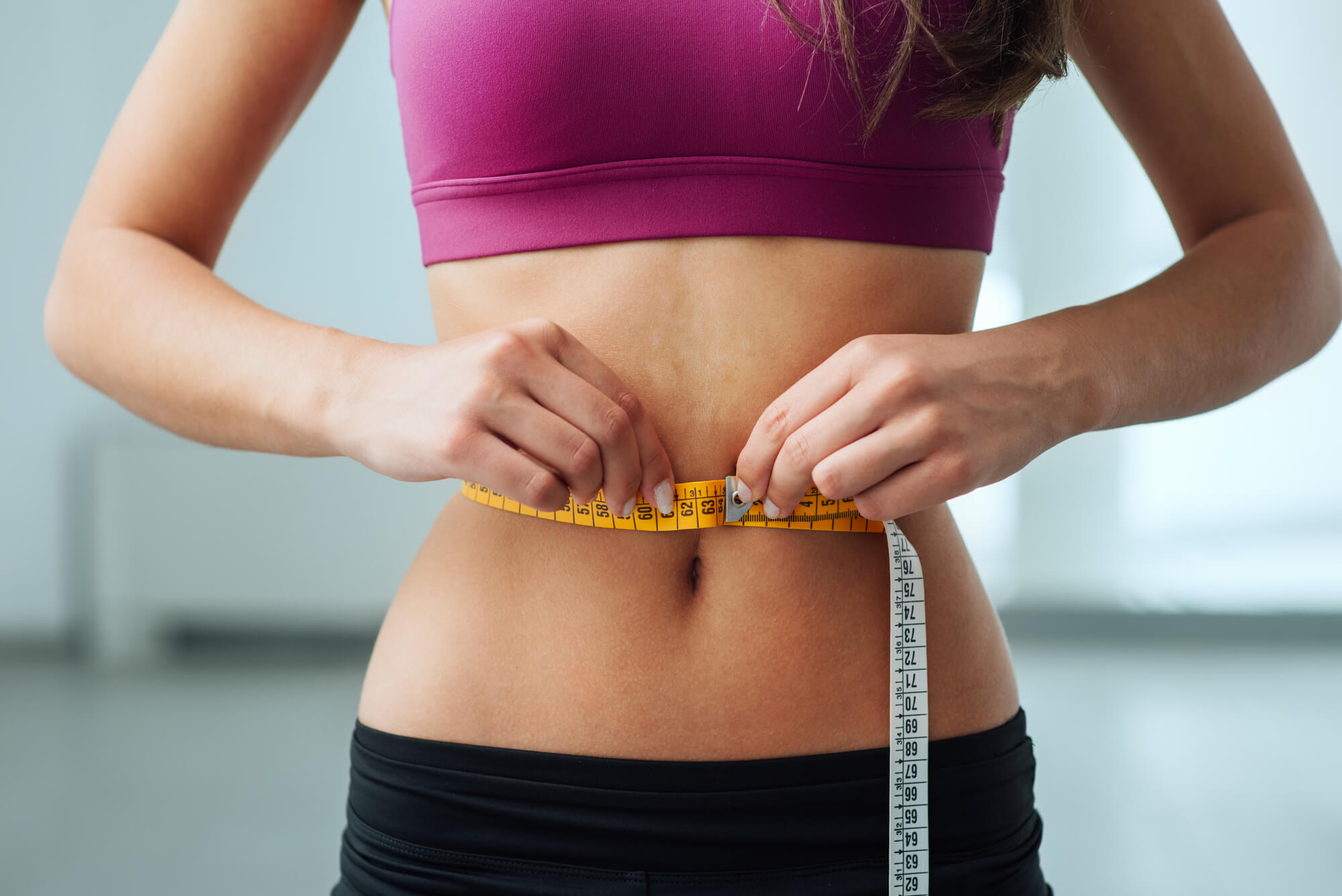 A woman holding a tape measure over her waist after undergoing weight loss in Palm Beach Gardens